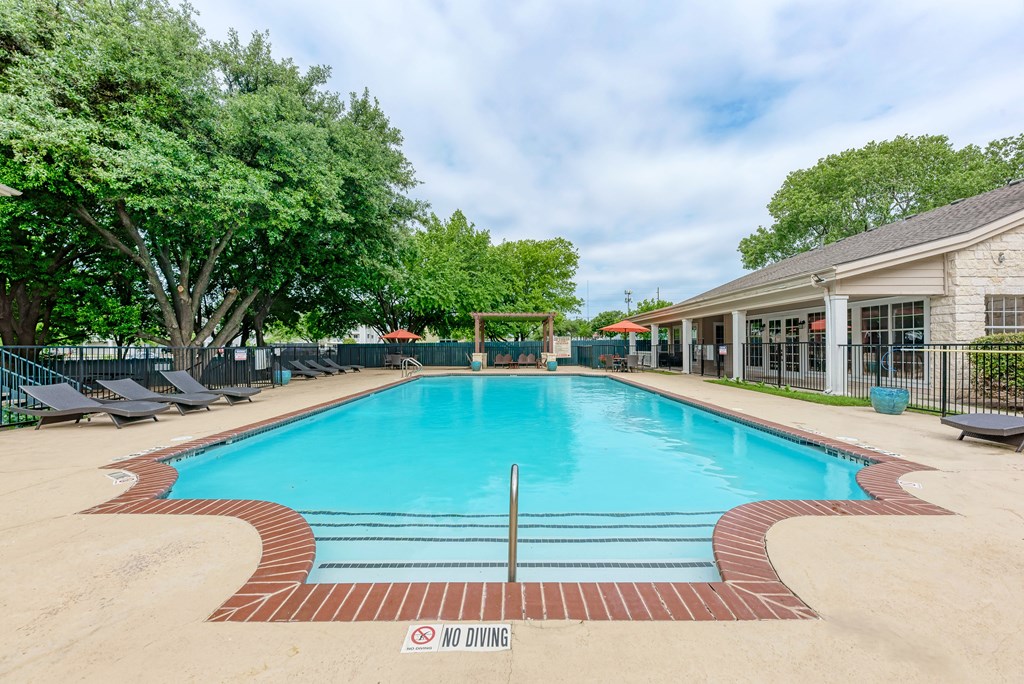 A large outdoor swimming pool surrounded by trees and lounge chairs.
