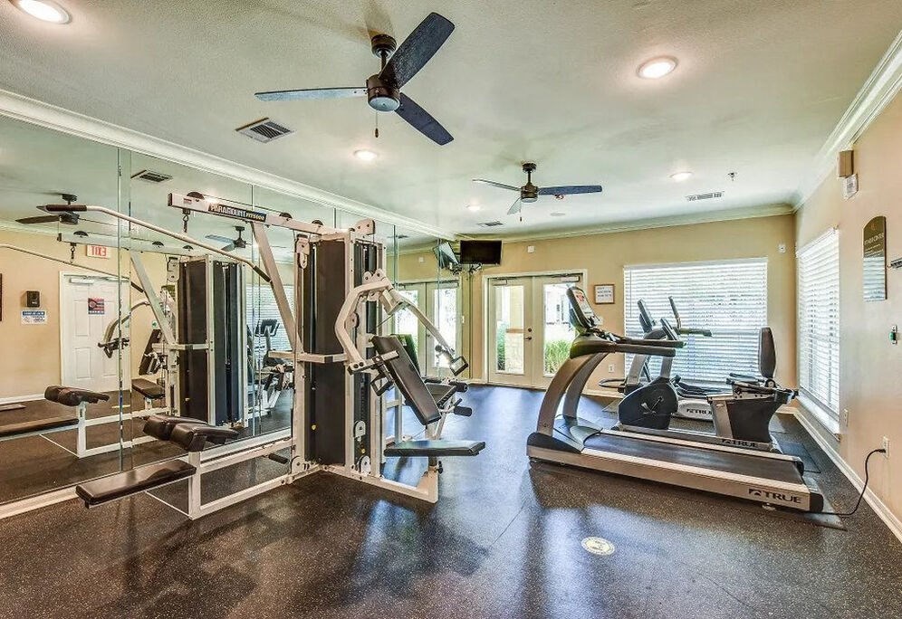 A spacious home gym with a variety of equipment including a treadmill, a stationary bike, and a weight bench.