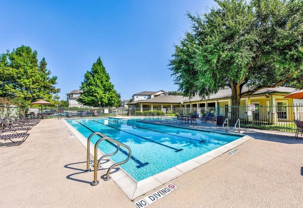 A swimming pool surrounded by trees and a building in the background.