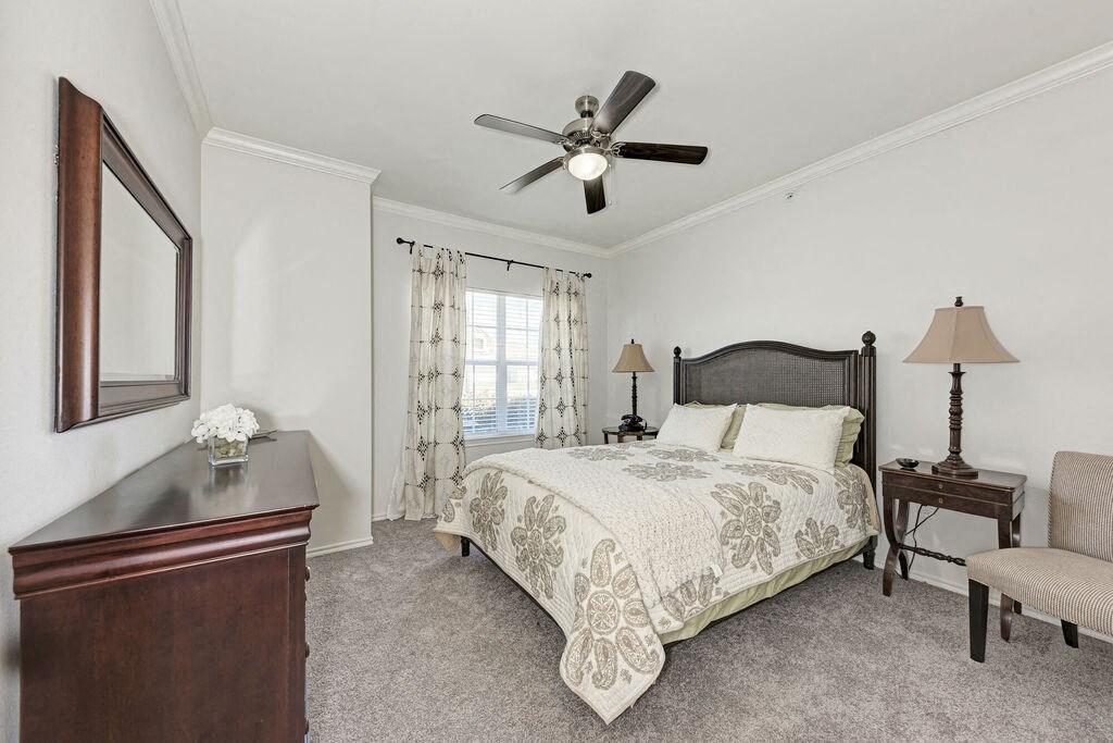 A bedroom with a bed, chair, and a ceiling fan.