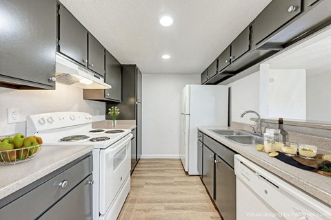 A kitchen with white appliances and a bowl of green apples on the counter.