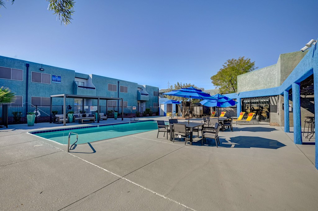 A pool area with a blue umbrella and chairs.