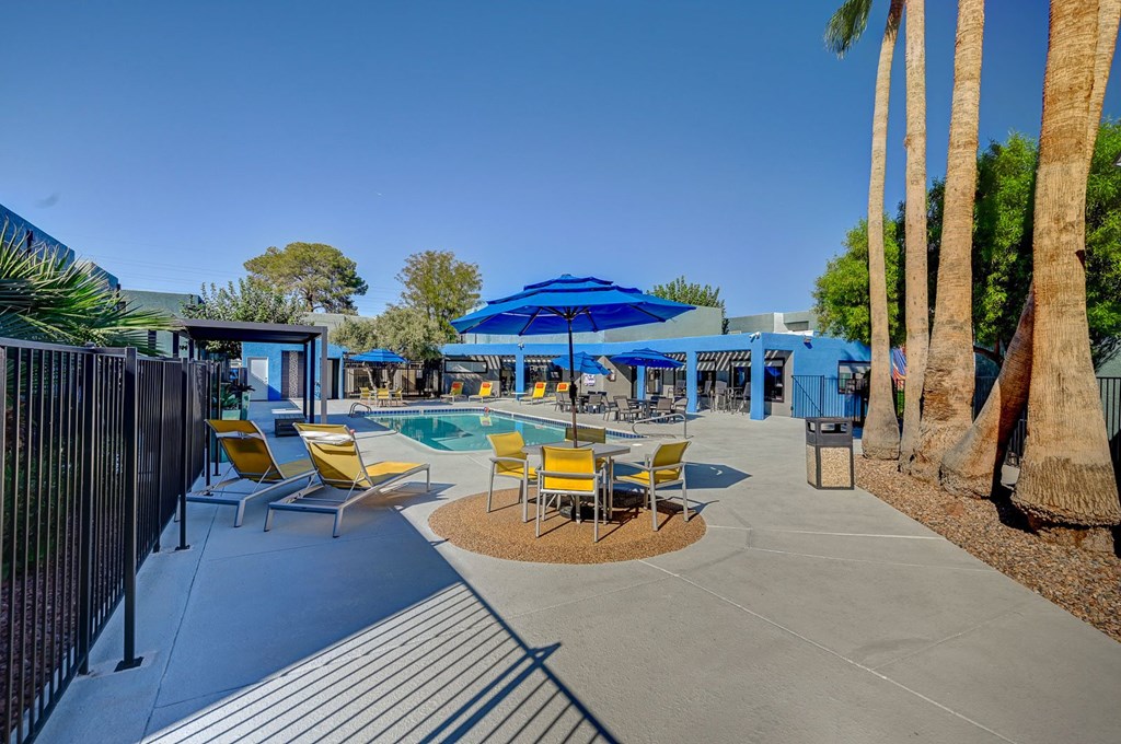 A pool area with a blue umbrella and yellow chairs.