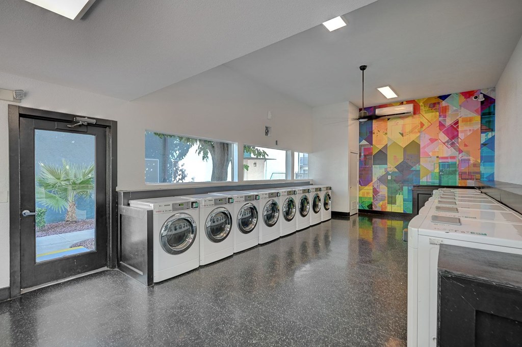 A laundry room with a row of washing machines and a colorful mosaic wall.