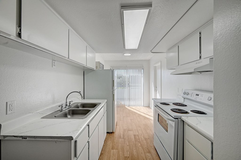 A white kitchen with a stove, sink, and cabinets.