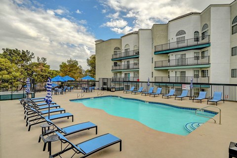 A swimming pool surrounded by sun loungers and apartment buildings.