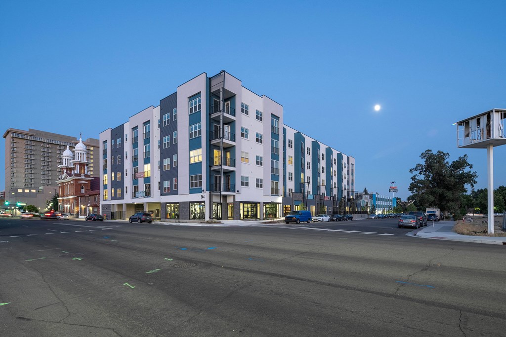 A modern multi-story building with a parking lot in front.