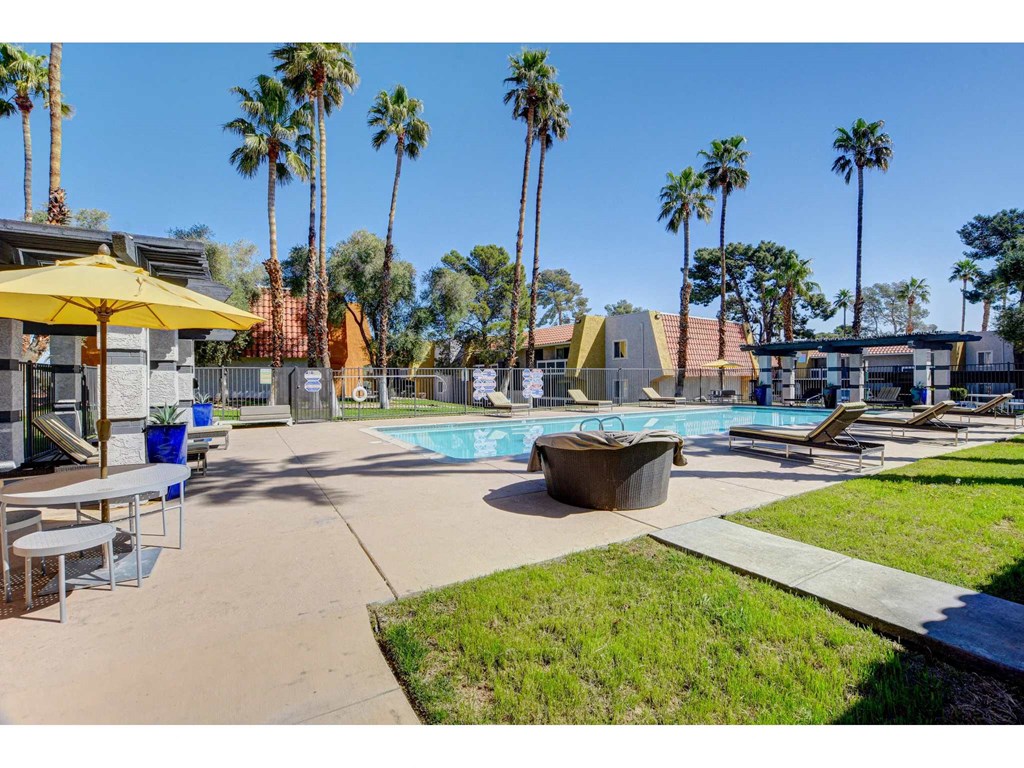 A pool area with a yellow umbrella and palm trees.
