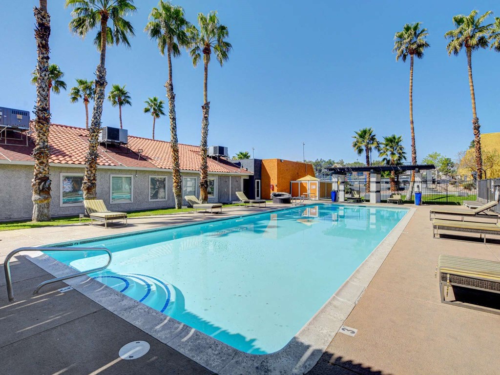 A pool surrounded by palm trees and a building in the background.