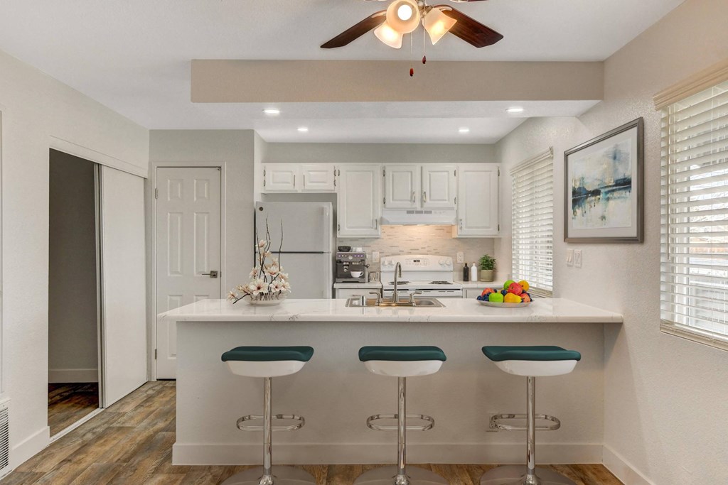 A kitchen with white cabinets and a white island with green bar stools.