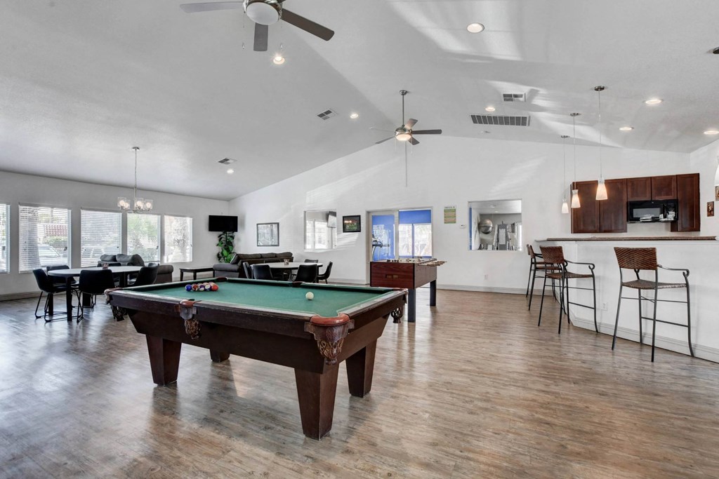 A pool table is in the middle of a room with a bar area.