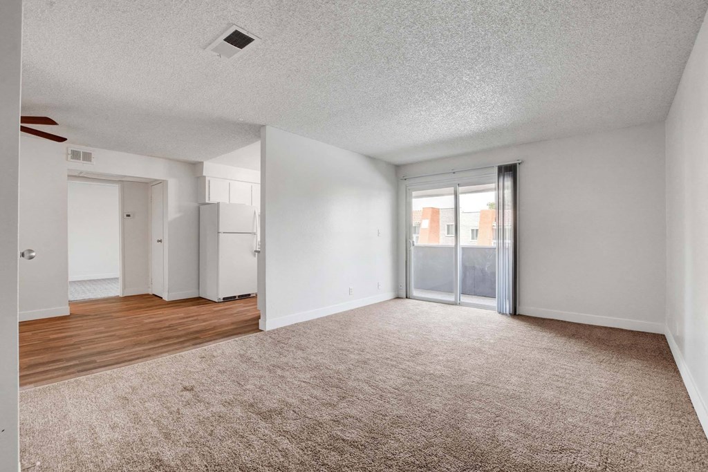 A spacious room with a carpeted floor and a sliding glass door leading to a balcony.