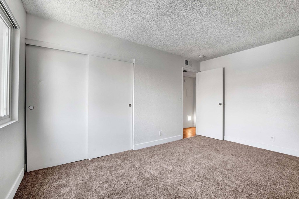 A room with carpeted floor and white walls with a door on the left.