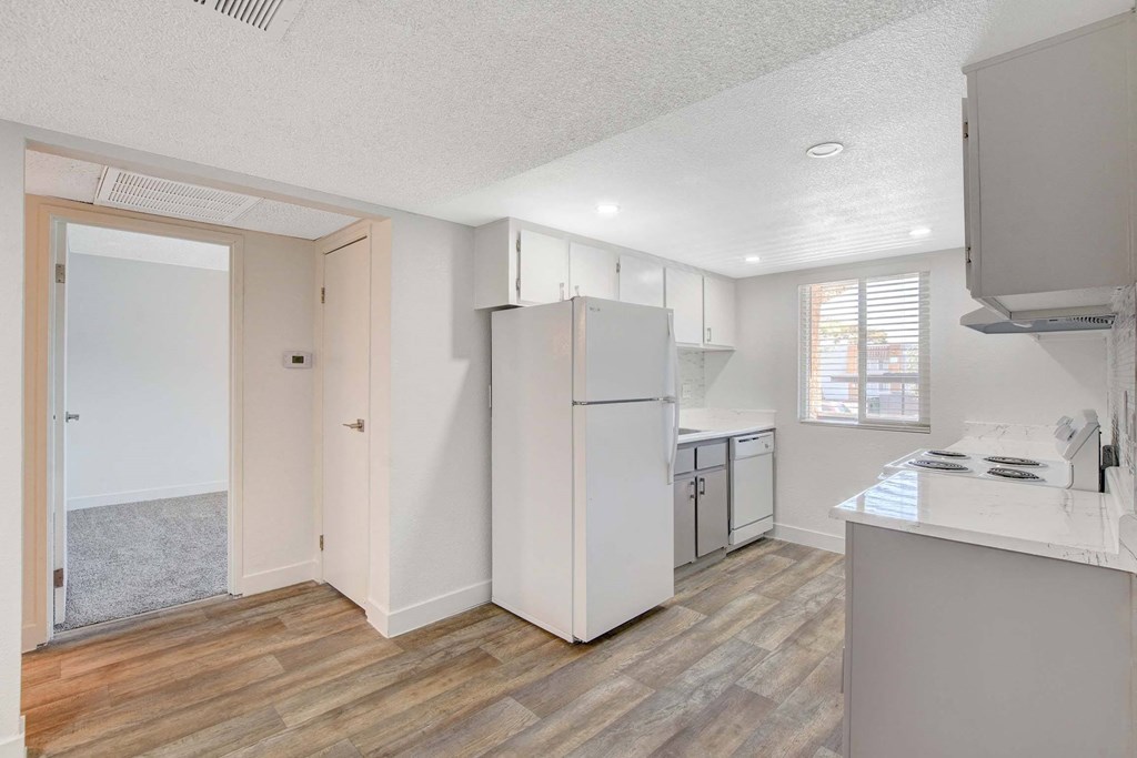 A kitchen with a white fridge and wooden floors.