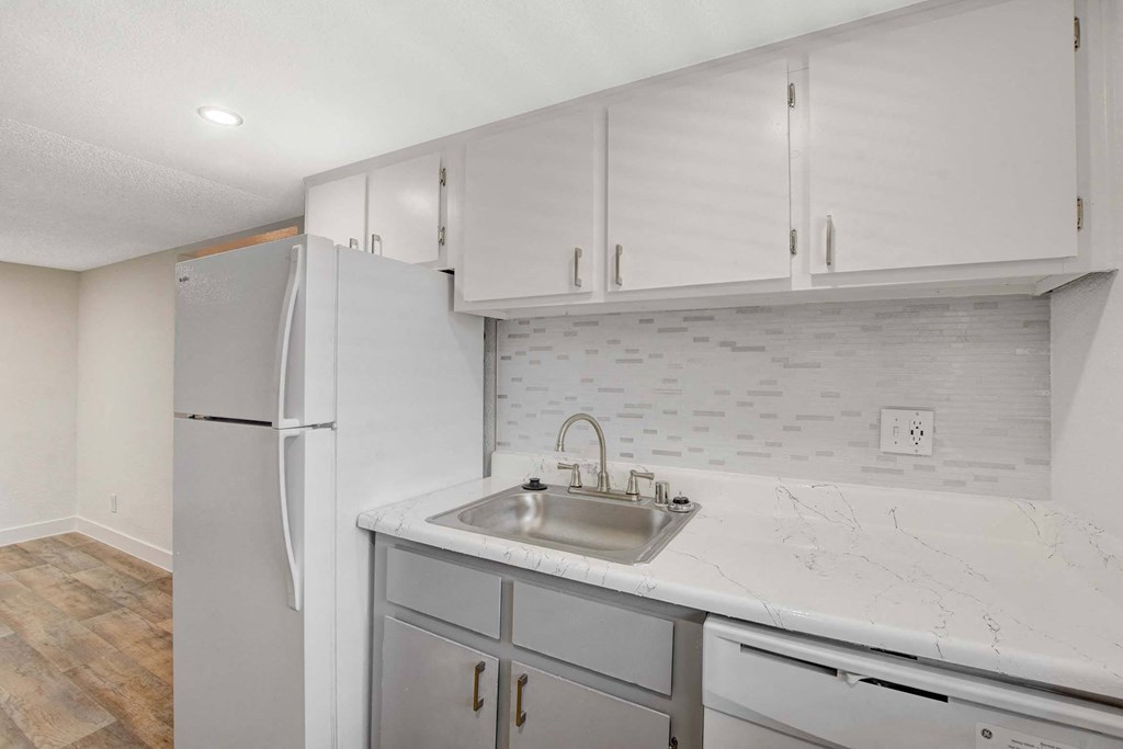 A kitchen with a white refrigerator, marble countertops, and wooden flooring.