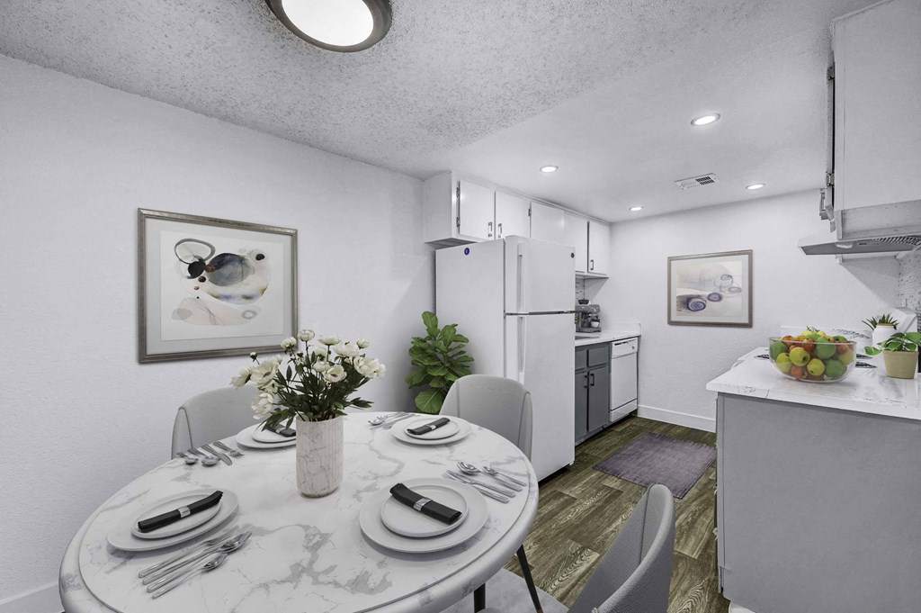 A dining room with a table set for two and a kitchen area in the background.