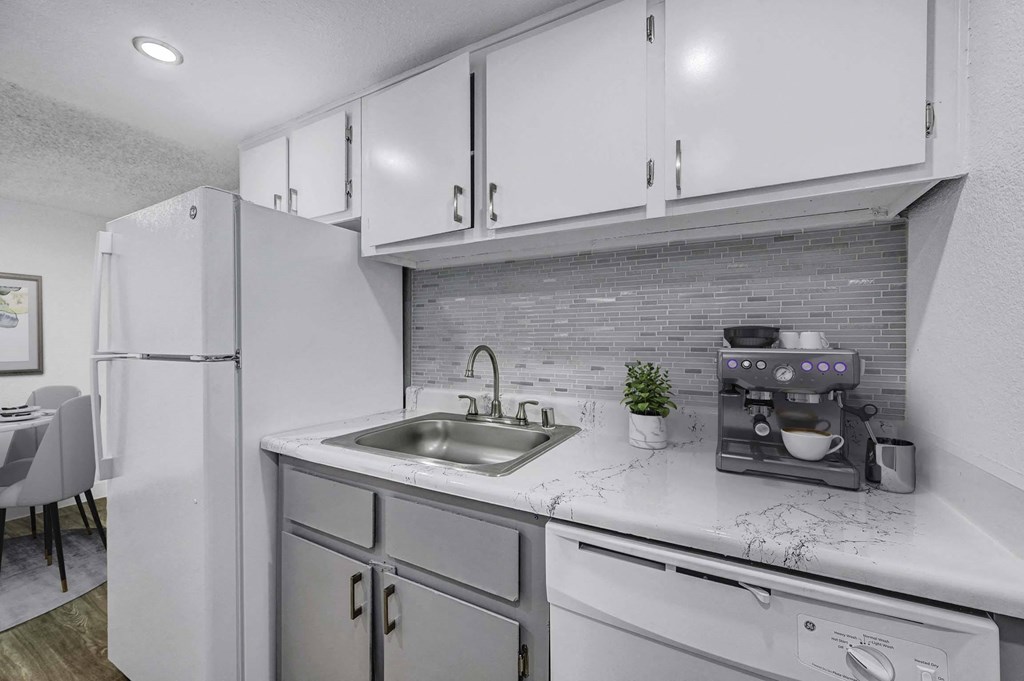 A modern kitchen with a white refrigerator, grey cabinets, and a marble countertop.
