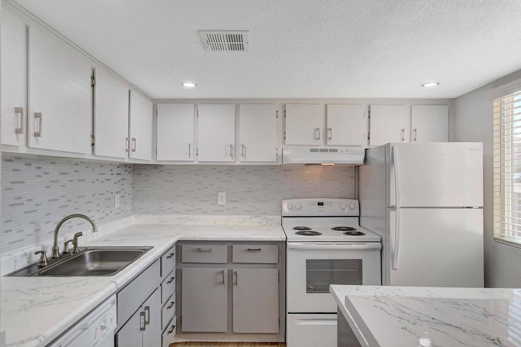 A kitchen with white cabinets and a marble countertop.