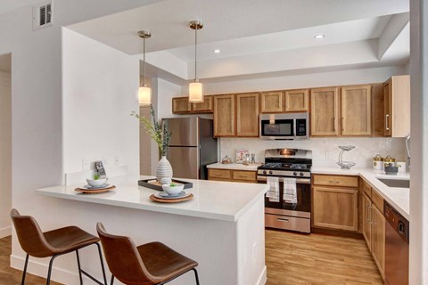 A kitchen with wooden cabinets and a white island with two chairs.