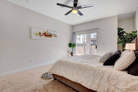 A bedroom with a bed, a ceiling fan, and a painting on the wall.