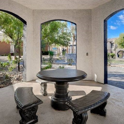 A table and two benches are in the foreground of a patio with arched openings.