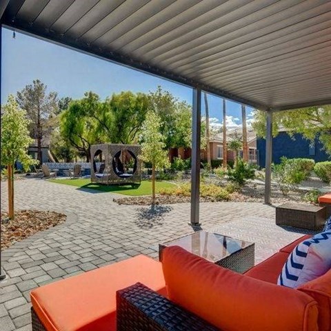 A patio with a couch and a table with a view of a garden and a building.