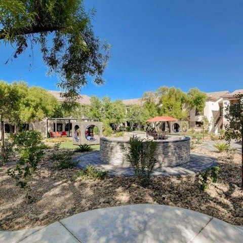 A garden with a fountain and a building in the background.