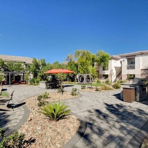 A sunny day at a courtyard with a red umbrella and a circular bench.