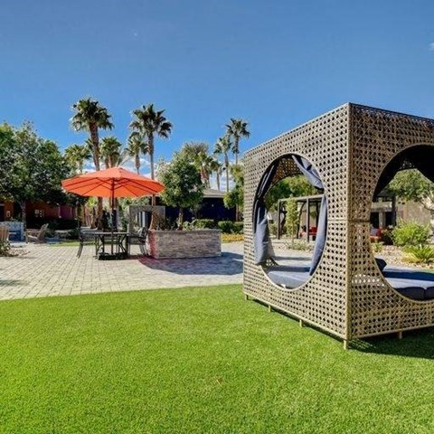 A modern outdoor seating area with a woven structure and a red umbrella.