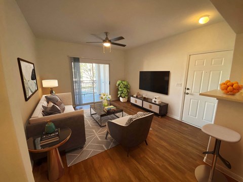 A living room with a brown sofa, a white armchair, a coffee table, a television, and a ceiling fan.