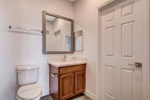 A bathroom with a toilet, sink, mirror, and door.
