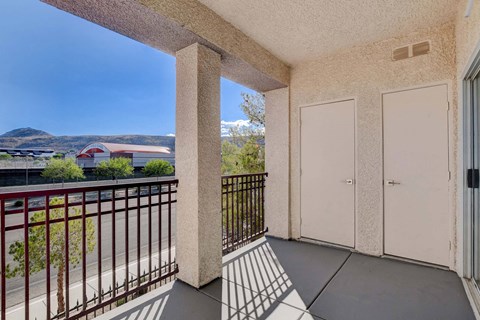 A balcony with a metal railing and a view of a red building and greenery.