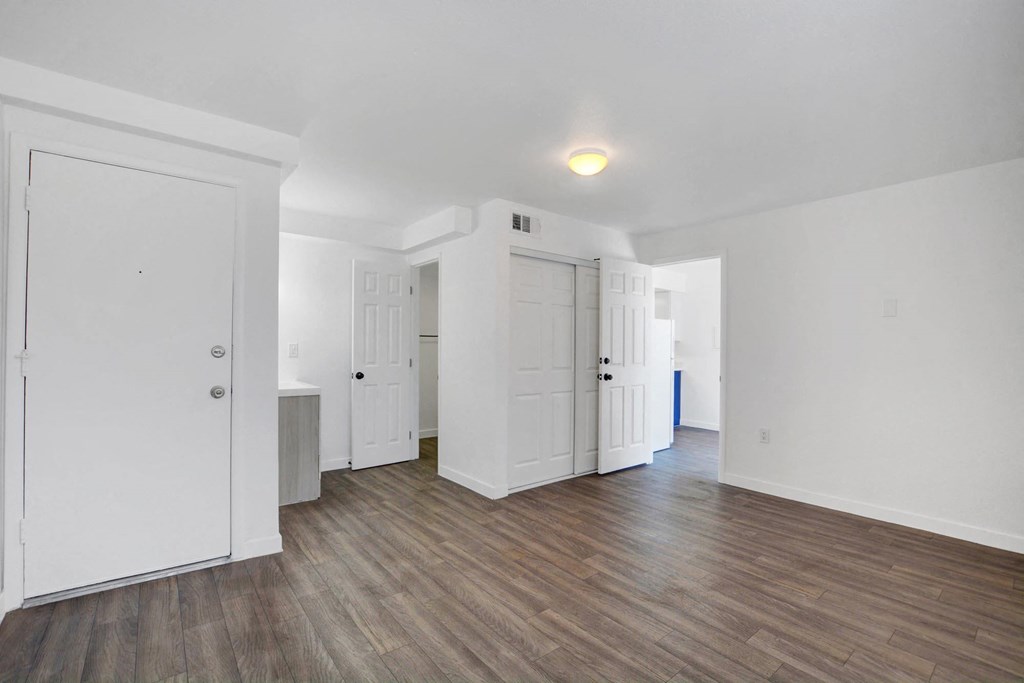 A room with white walls and wooden flooring with a door on the left.