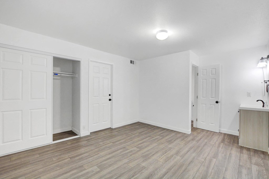 A room with white walls and wooden flooring, featuring a door, a window, and a light fixture.
