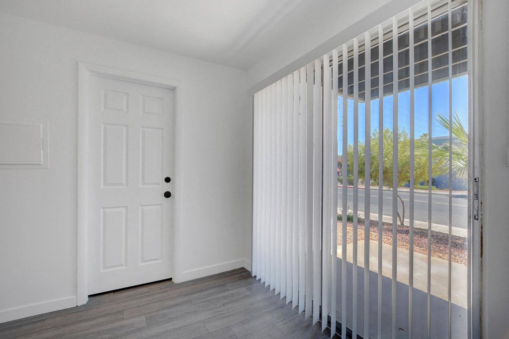 A white door with a black handle is in a room with a window covered with white blinds.