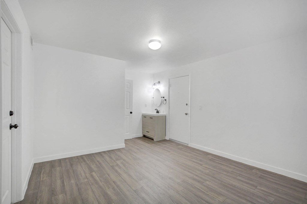 A room with a wooden floor and a white wall with a cabinet and a mirror.