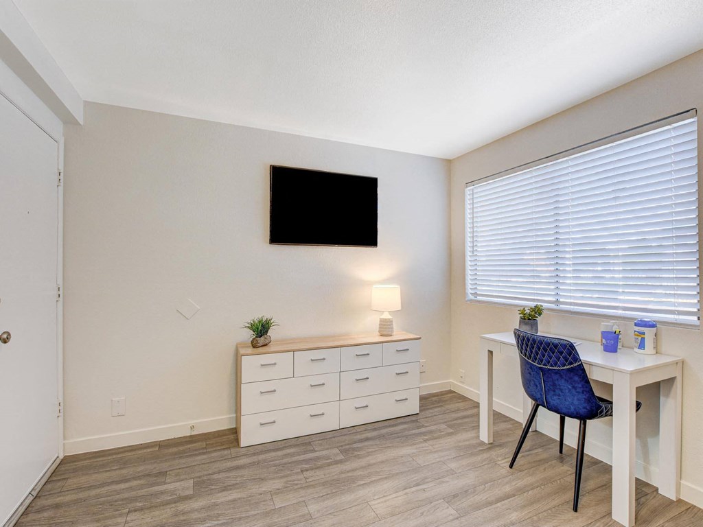 A room with a desk, chair, and a television mounted on the wall.