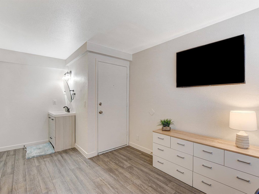 A room with a white door, a black screen on the wall, and a wooden bench with drawers underneath it.