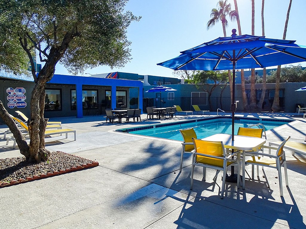 A pool area with a blue umbrella and yellow chairs.