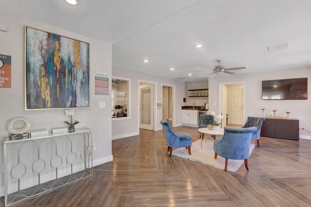 A living room with a blue chair and a painting on the wall.