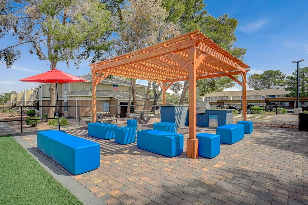 A pavilion with a red umbrella and blue seating is surrounded by trees.
