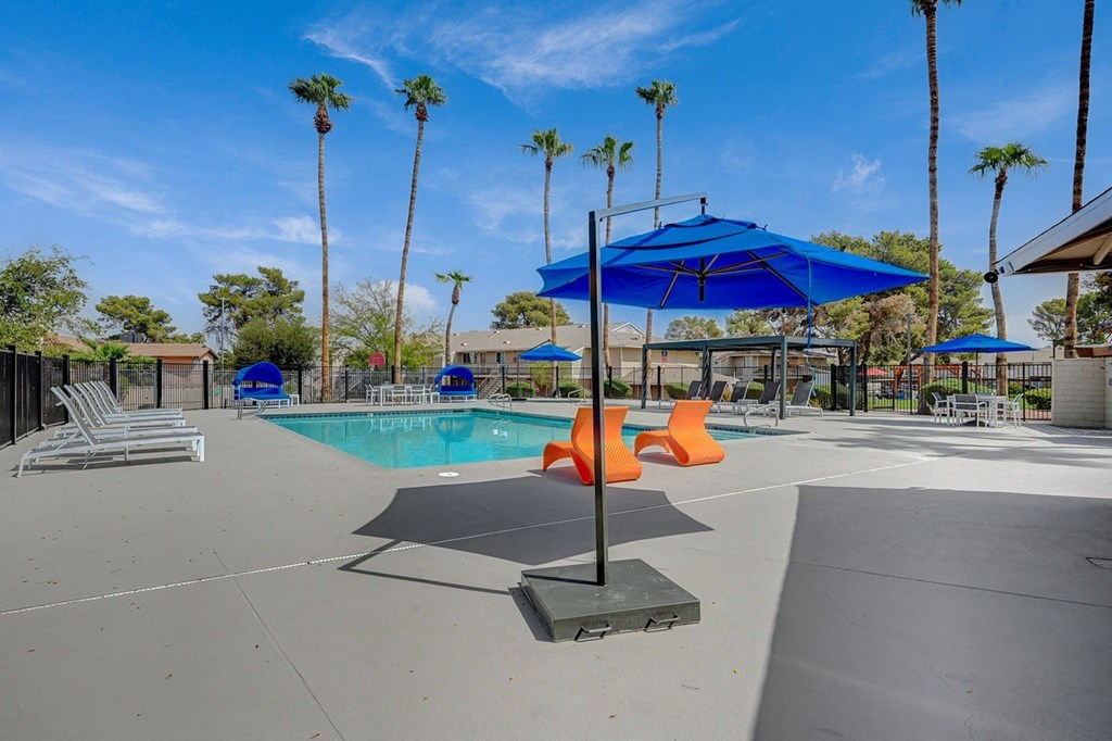 A pool area with a blue umbrella and orange chairs.