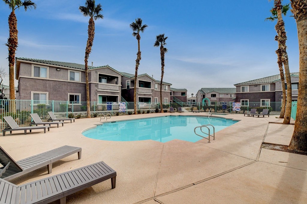A pool surrounded by palm trees and lounge chairs.