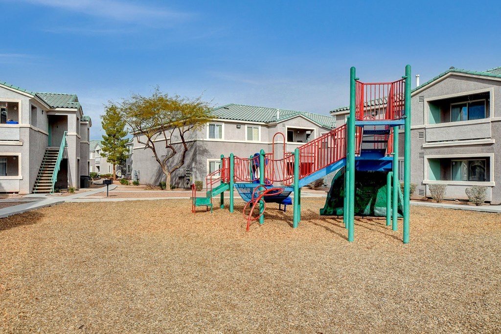 A playground with a red and blue slide in front of apartment buildings.