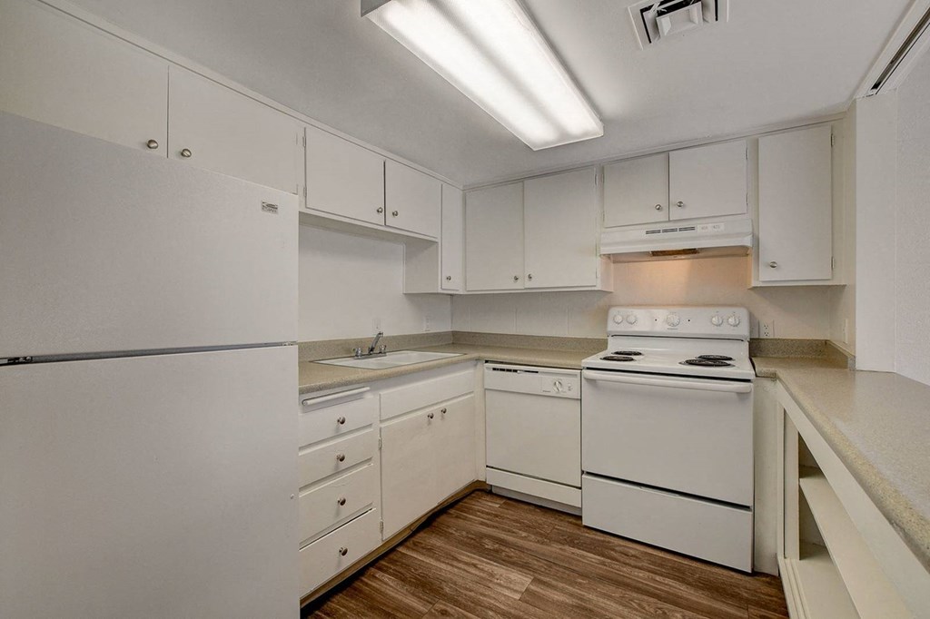 A white kitchen with a stove, sink, and cabinets.