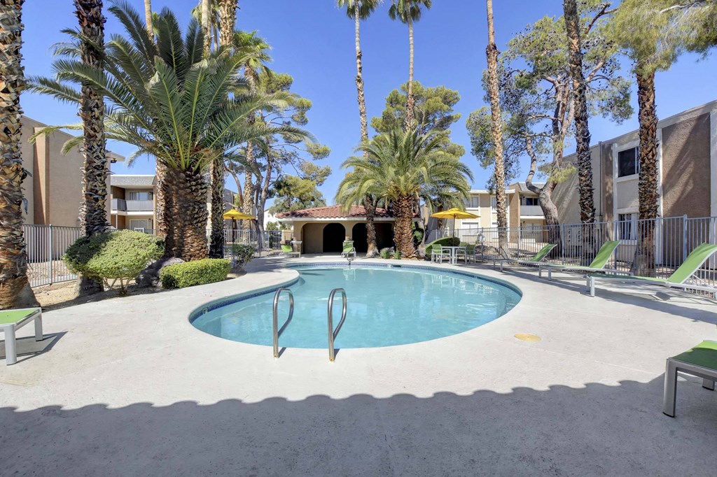 A pool surrounded by palm trees and lounge chairs.