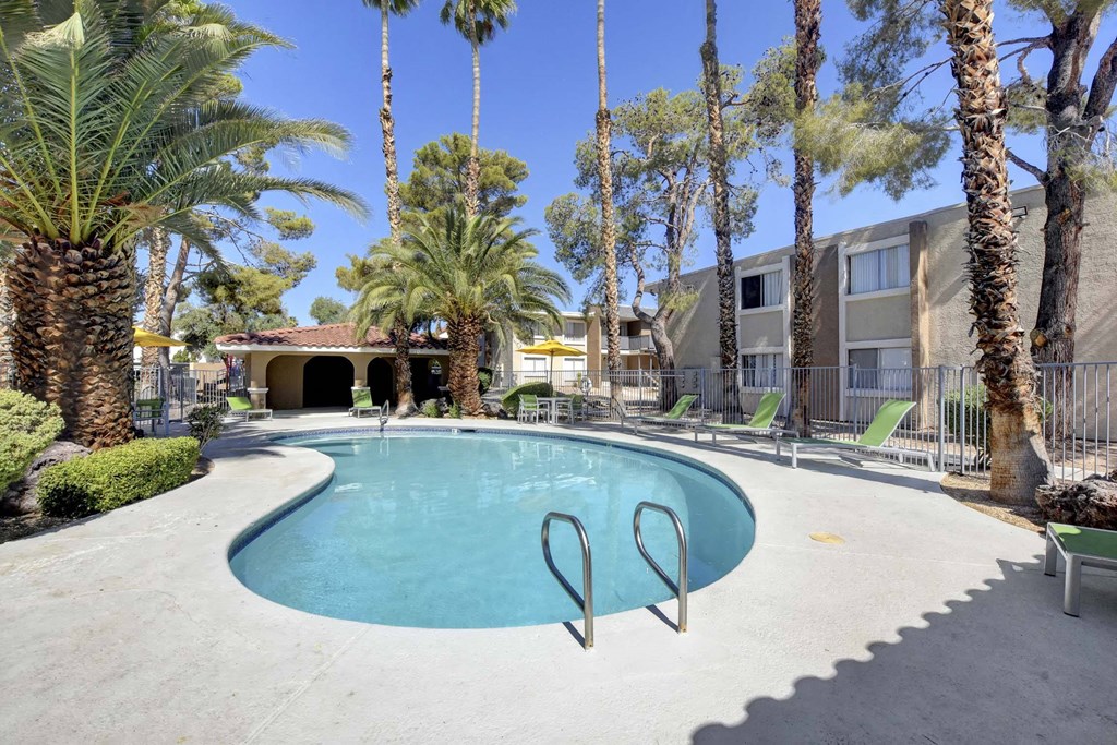 A pool surrounded by palm trees and a building in the background.