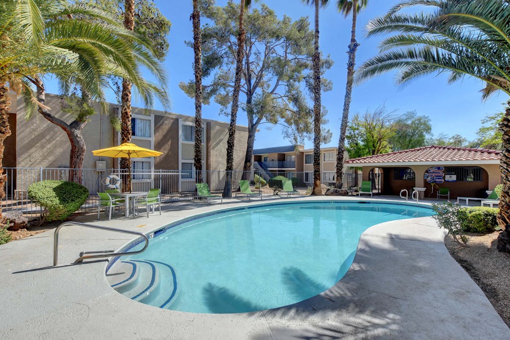 A pool surrounded by palm trees and a yellow umbrella.