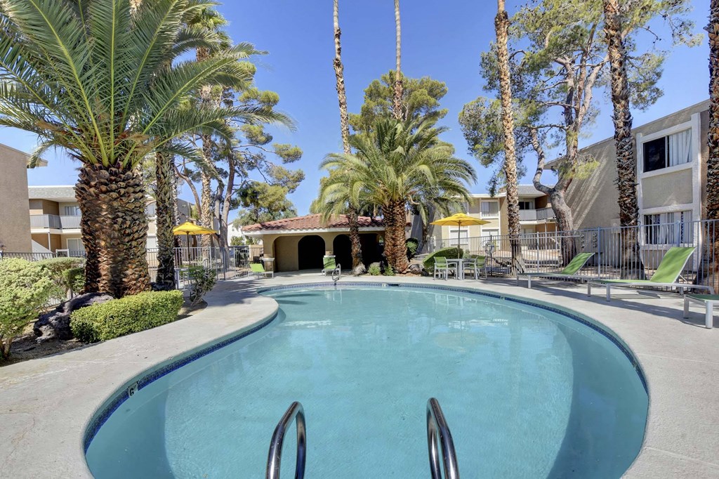 A swimming pool surrounded by palm trees and a building in the background.