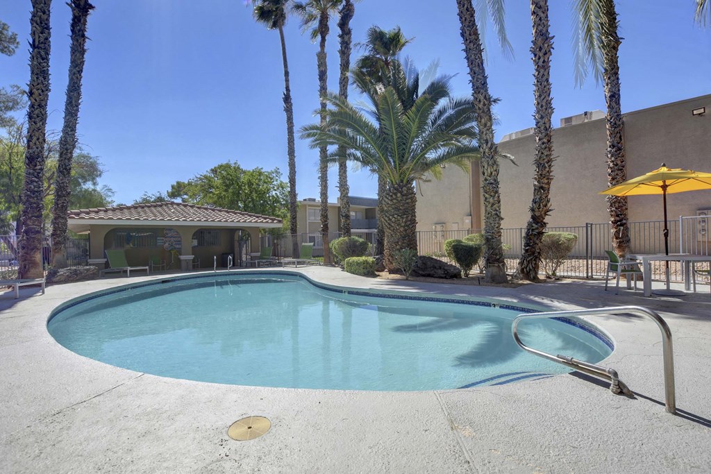 A pool surrounded by palm trees and a building in the background.